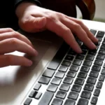 Mãos utilizando o teclado de um notebook sobre a mesa